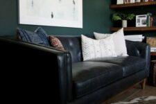 a moody home office with dark green walls, a black leather sofa, a faux fur rug and stained wooden shelves