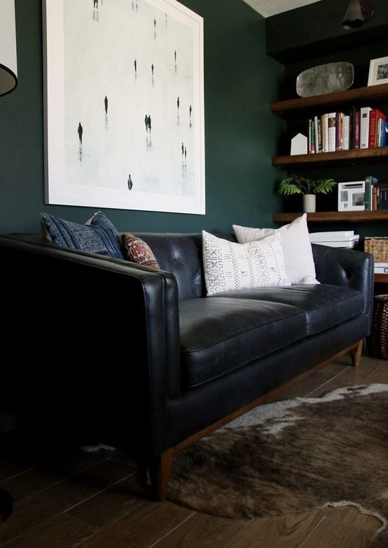 a moody home office with dark green walls, a black leather sofa, a faux fur rug and stained wooden shelves