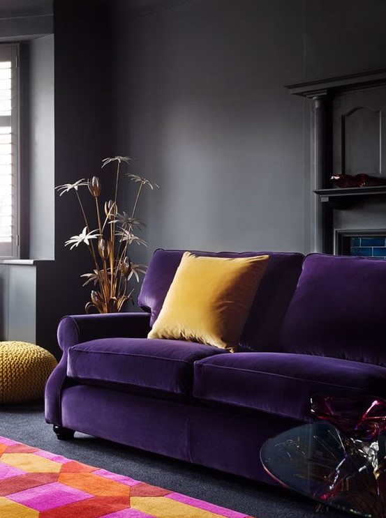 a moody living room in dark greys spruced up with a deep violet sofa, yellow pillows and a colorful geometric rug