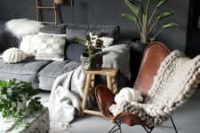 a moody living room with a grey low sofa, a graphite grey accent wall, a brown leather butterfly chair, a low coffee table