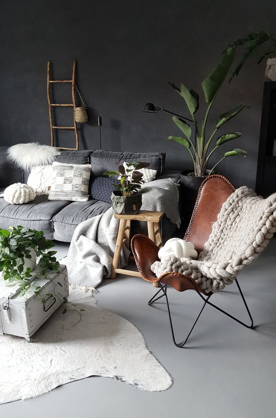a moody living room with a grey low sofa, a graphite grey accent wall, a brown leather butterfly chair, a low coffee table