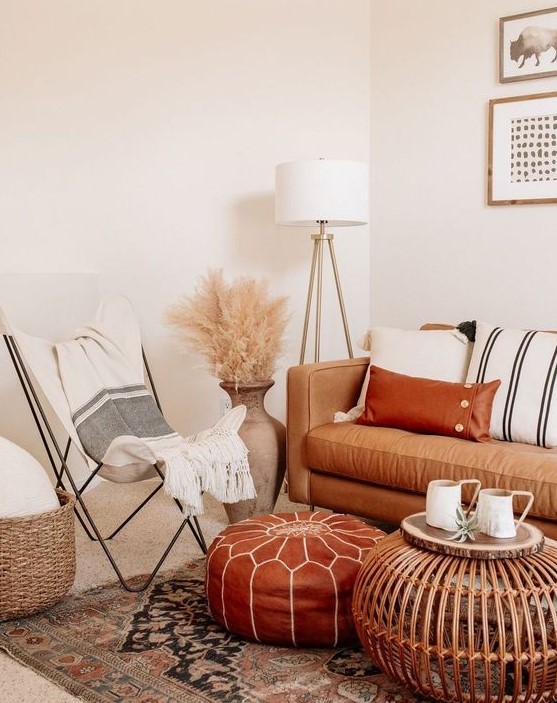 a neutral boho space with a tan leather sofa and a rust-colored ottoman, striped textiles, pampas grass and a wooden table