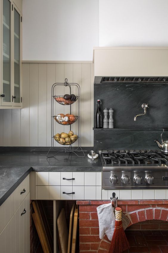 a neutral cottage kitchen with beadboard cabinets, a grey soapstone backsplash and countertops, black fixtures to support the look