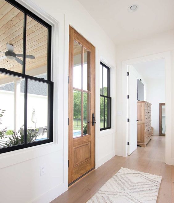 a neutral farmhouse entryway with a stained door, black double-hung windows, a printed rug is a cool space