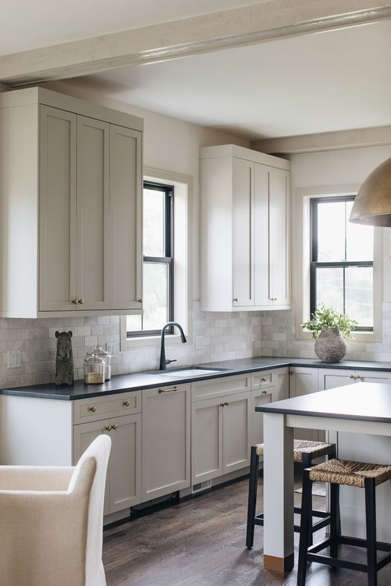 a neutral farmhouse kitchen with shaker cabinets, black countertops, a neutral tile backsplash, black double-hung windows and black fixtures