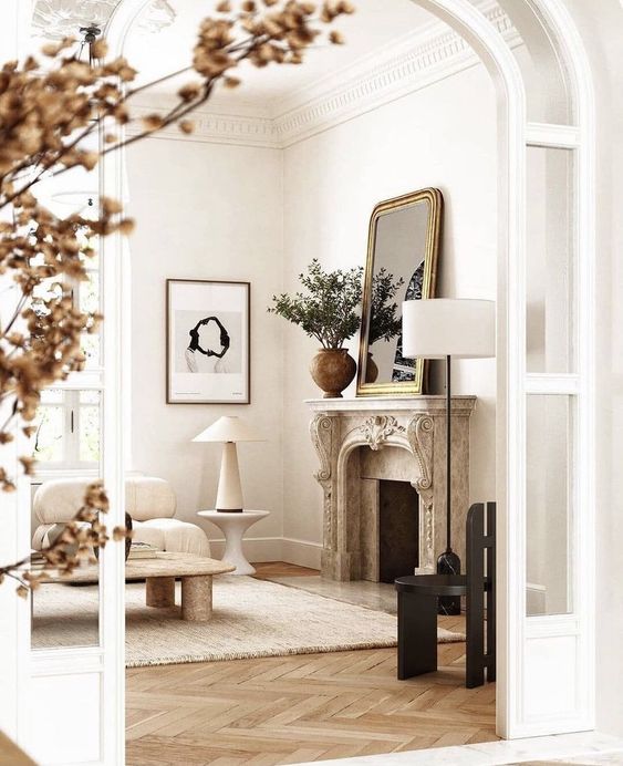 a neutral living room with a French fireplace, low seating furniture, a low coffee table, a mirror in a gilded frame and a black chair