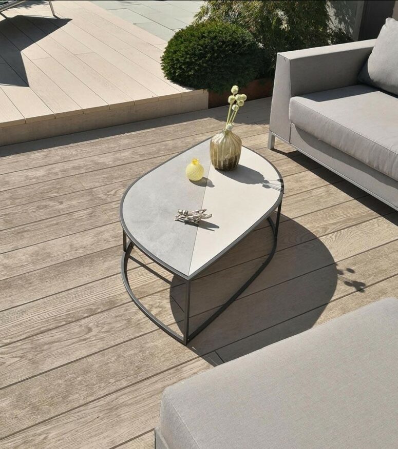 a neutral terrace with limed and gold oak decking, neutral upholstered furniture and a leaf-shaped coffee table with decor
