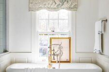 a neutral vintage bathroom with paneling, a large tub, a double-hung window, a printed curtain and an artwork