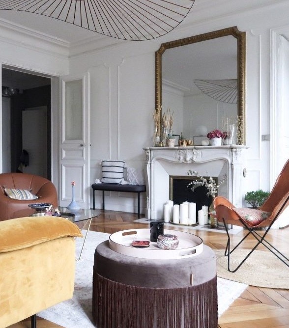 a pretty modern French chic living room with a French fireplace, leather and velvet furniture of earthy tones and an oversized mirror