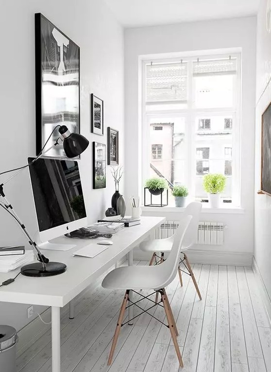a pretty white Nordic home office with a black and white gallery wall, a white shared desk, white Eames chairs and potted greenery