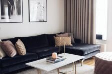 a refined living room with a black sectional, a coffee table with gold legs, a tufted ottoman, a gallery wlal and greige curtains