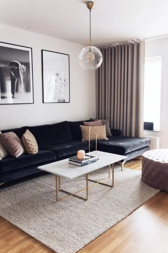 a refined living room with a black velvet sectional, a coffee table with gold legs, a tufted ottoman, a gallery wlal and greige curtains