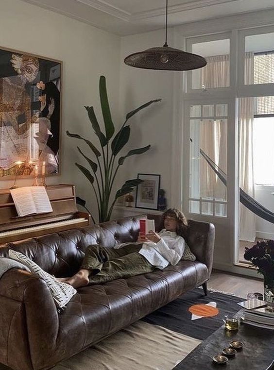 a refined living room with a dark brown leather sofa, a piano, a potted plant, a statement artwork and a coffee table