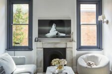 a refined living room with black frame double-hung windows, a fireplace, a large sectional, a white chair and a stone table