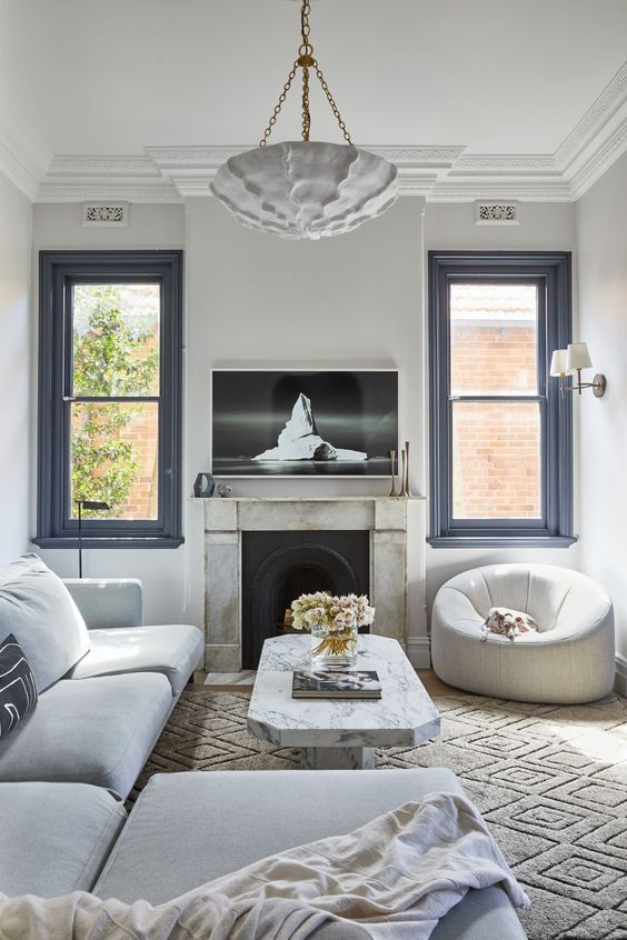 a refined living room with black frame double hung windows, a fireplace, a large sectional, a white chair and a stone table
