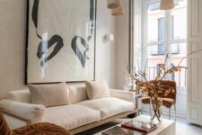 a refined modern living room with a neutral sofa, rust chairs, a low slab coffee table and a statement artwork plus pendant lamps