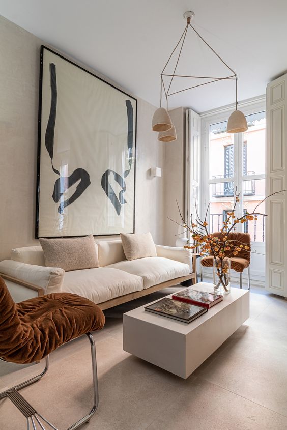 a refined modern living room with a neutral sofa, rust chairs, a low slab coffee table and a statement artwork plus pendant lamps