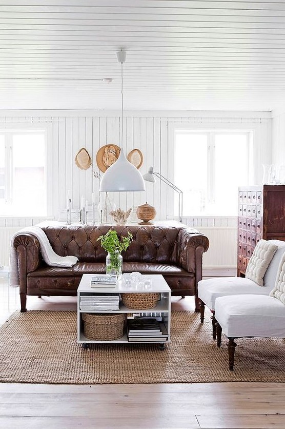 a refined rustic living room with a brown leather Chesterfield sofa, a vintage apothecary cabinet and white chairs