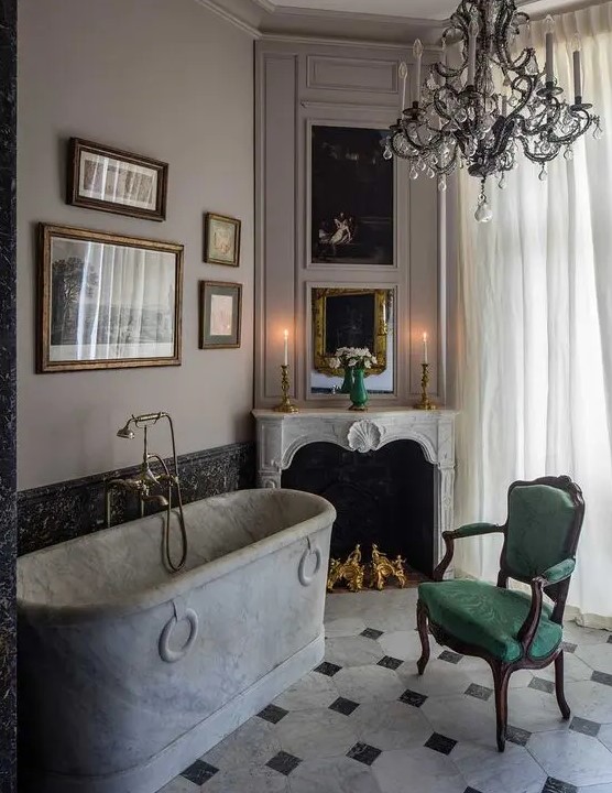 a refined vintage bathroom with a chic French fireplace, a marble bathtub, a black chandelier, a gallery wall and a green chair
