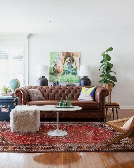a relaxed living room with a brown leather Chesterfield sofa, a woven chair, a fur stool and some plants