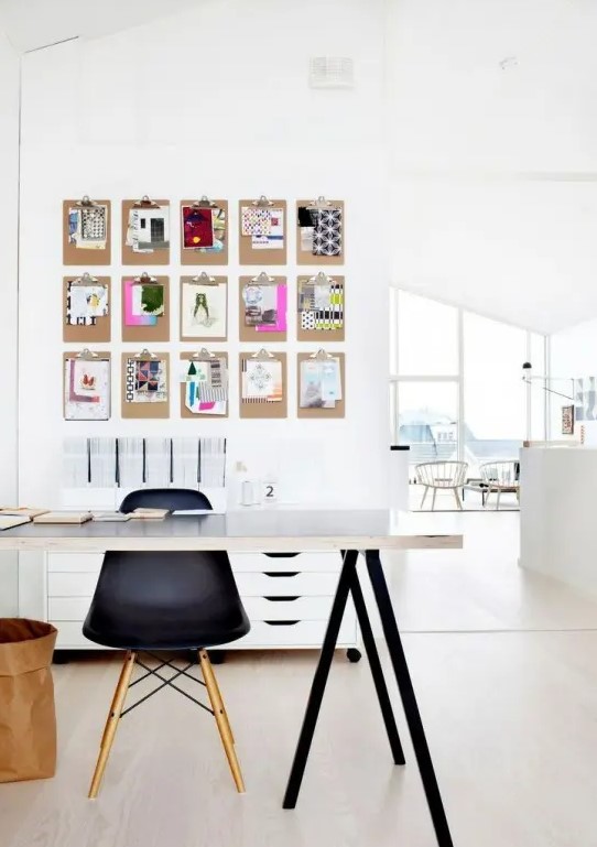 a small Scandi home office nook with a black and white trestle desk, a black Eames chair, a memo board a white file cabinet and a basket for storage