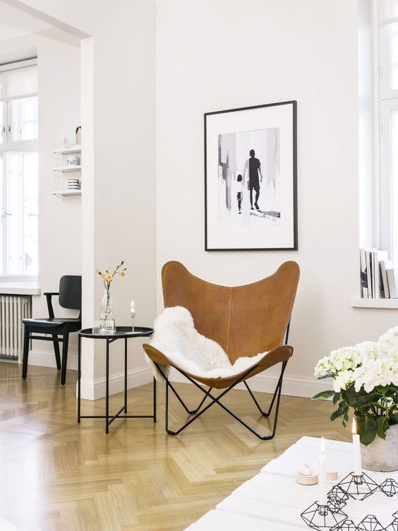 a small and cozy sitting nook with a brown leather butterfly chair, a side table with decor and an artwork is chic
