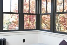 a small and cozy sunroom done with rows of double-hung windows with black framing and a cozy daybed