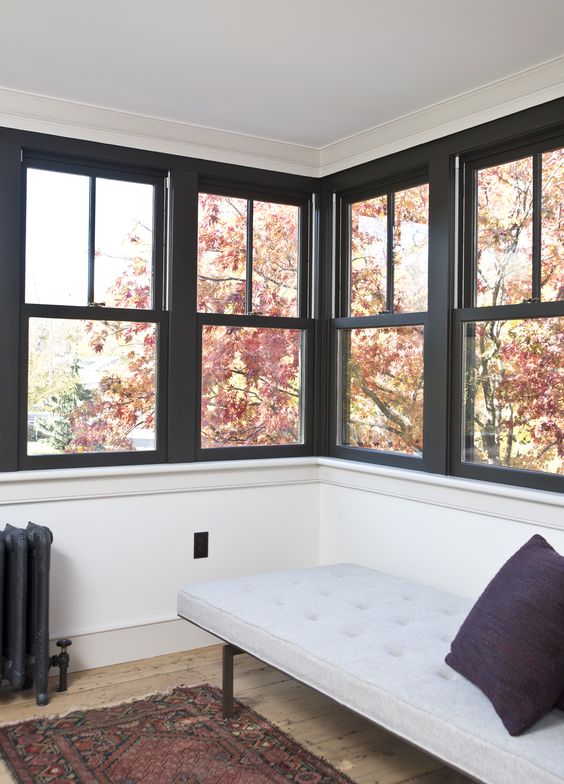 a small and cozy sunroom done with rows of double hung windows with black framing and a cozy daybed