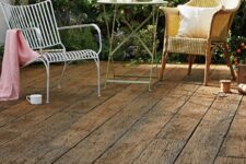 a small and cute outdoor space done with weathered oak, with a metal coffee table anda woven and a metal chair plus greenery in the backdrop