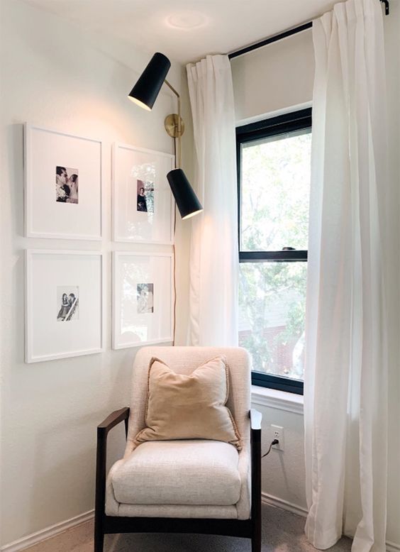 a small reading nook with a black frame double-hung window, a neutral chair with black framing, a grid gallery wall