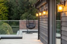 a small terrace clad with burnt cedar millboard decking and smoked oak decking that contrast the darker walls and a dark egg-shaped chair