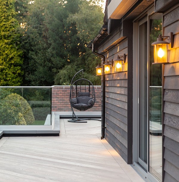 a small terrace clad with burnt cedar millboard decking and smoked oak decking that contrast the darker walls and a dark egg shaped chair
