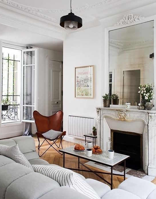 a small yet chic French style living room with a French fireplace, a coffee table, a brown butterfly chair and a grey sofa