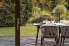 a sophisitcated modern terrace clad with antique oak composite decking, with a modern dining table and an upholstered bench plus a beautiful garden next to the deck