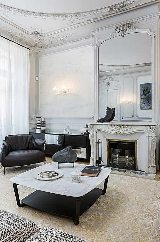 a sophisticated French living room with molding on the ceiling, black leather furniture, a low coffee table, a French fireplace
