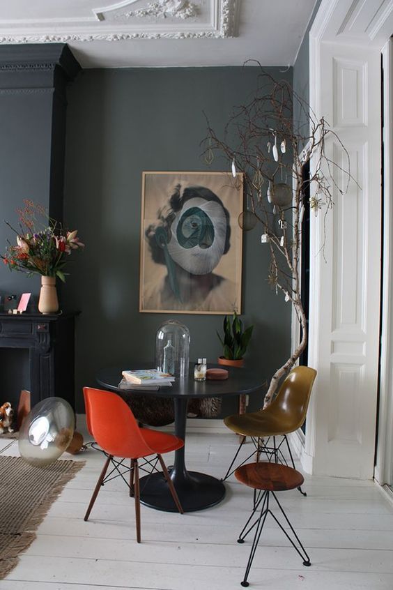 a sophisticated and dramatic space with a black table, an orange and mustard Eames chair, black walls and a fireplace