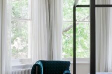 a sophisticated bedroom with arched double-hung windows, a black canopy bed, a teal chair and a side table