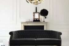 a sophisticated black and white living room with a non-working fireplace, a refined black Chesterfield sofa, a creative glam gold coffee table and a brass chandelier