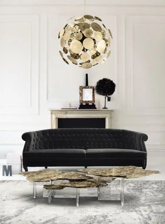 a sophisticated black and white living room with a non-working fireplace, a refined black Chesterfield sofa, a creative glam gold coffee table and a brass chandelier