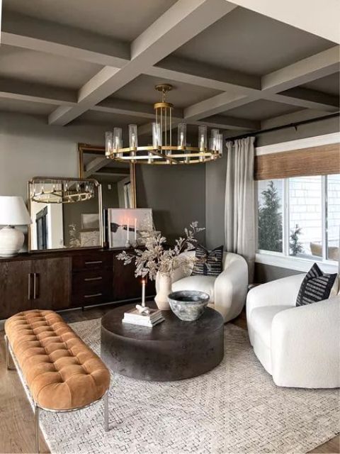 a sophisticated living room in earthy tones, with grey walls and a ceiling, a dark stained credenza, white chairs, a round coffee table and a rust colored upholstered bench