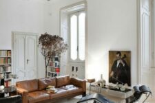a sophisticated living room with a black and amber leather sofa, a black leather lounger, a coffee table, a statement artwork and booksehvles