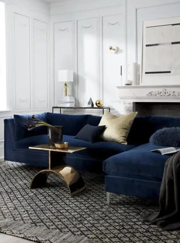 a sophisticated living room with paneling, a vintage fireplace, a midnight blue sofa, navy and gold pillows, a gold side table and some table lamps