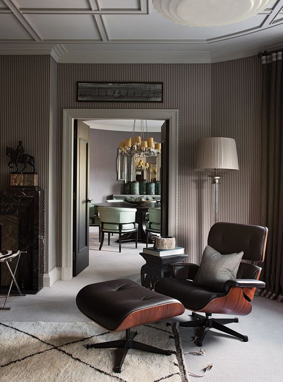 a sophisticated space with a black Eames lounger and ottoman, taupe walls, a chic floor lamp and a cool ceiling