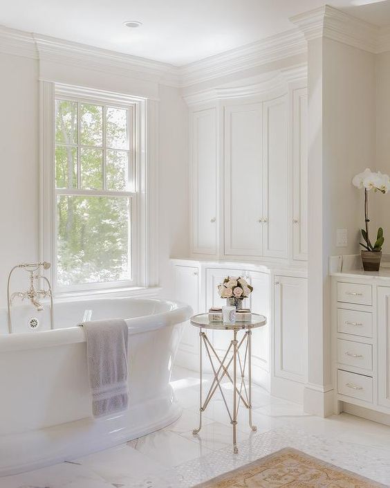 a sophisticated vintage bathroom with a double-hung window, built-in cabinets, an oval tub and a side table