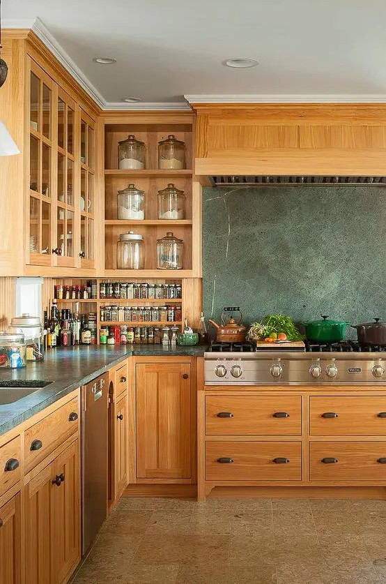 a stained kitchen with flat panel and shaker cabinets, grey soapstone countertops and a blacksplash, stainless steel countertops