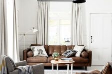 a stylish Scandinavian living room with a brown leather sofa, a grey chair and a woven one, a coffee table and a black pendant lamp