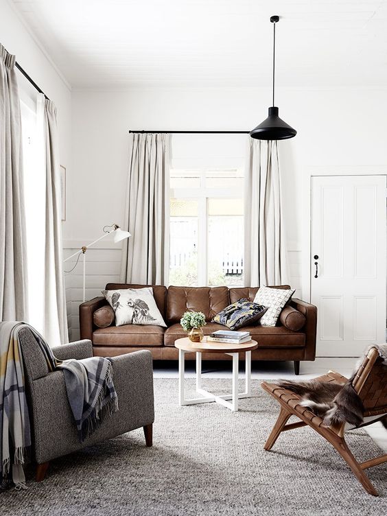 a stylish Scandinavian living room with a brown leather sofa, a grey chair and a woven one, a coffee table and a black pendant lamp