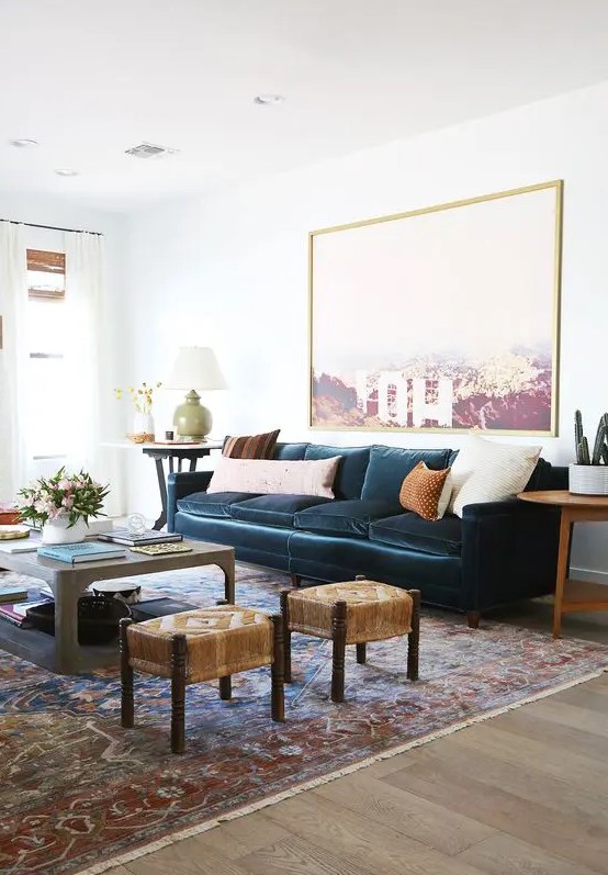 a stylish and elegant living room with a navy vlevet sofa, a statement artwork, a coffee table and woven stools, neutral pillows