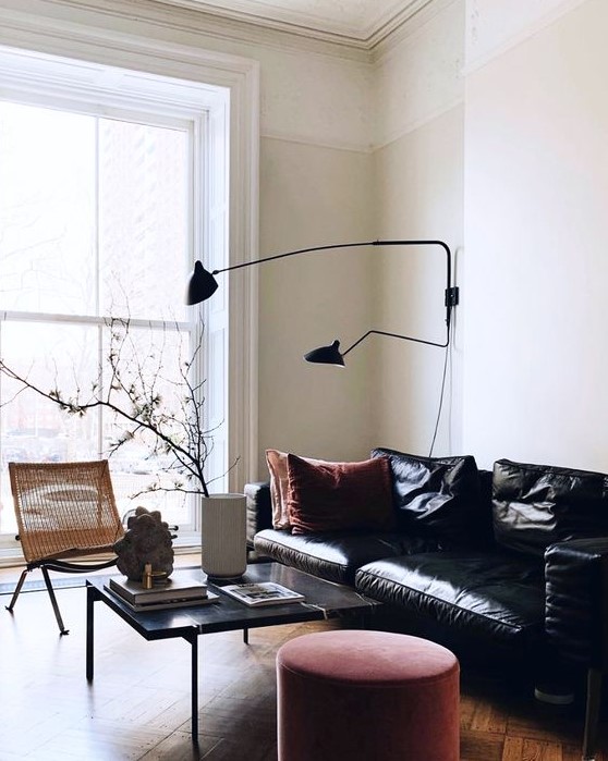 a stylish and refined living room with a black leather sofa, a red velvet ottoman and a wicker lounger