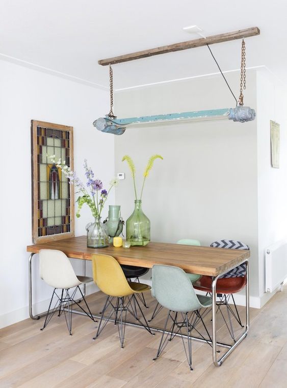 a stylish dining space with a long dining table, colorful Eames chairs, a mosaic artwork and a catchy lamp on chain